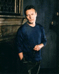 Tony in blue, standing in front of fireplace